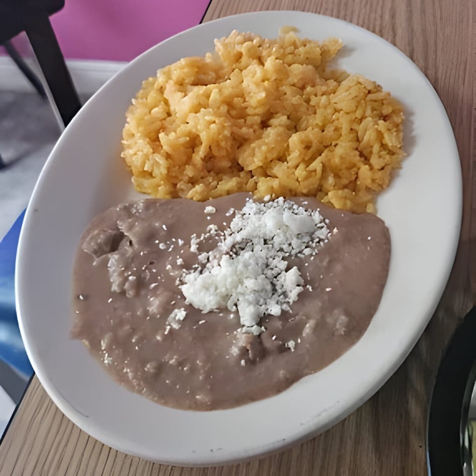 A white plate of Las Flores Mexican refried beans topped with cheese and yellow rice.