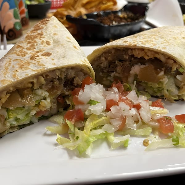 A large, cut burrito on a white plate, revealing its filling of meat, rice, and lettuce.