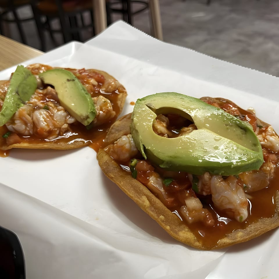 Two shrimp tostadas with red sauce and avocado slices on white paper at Las Flores Mexican.