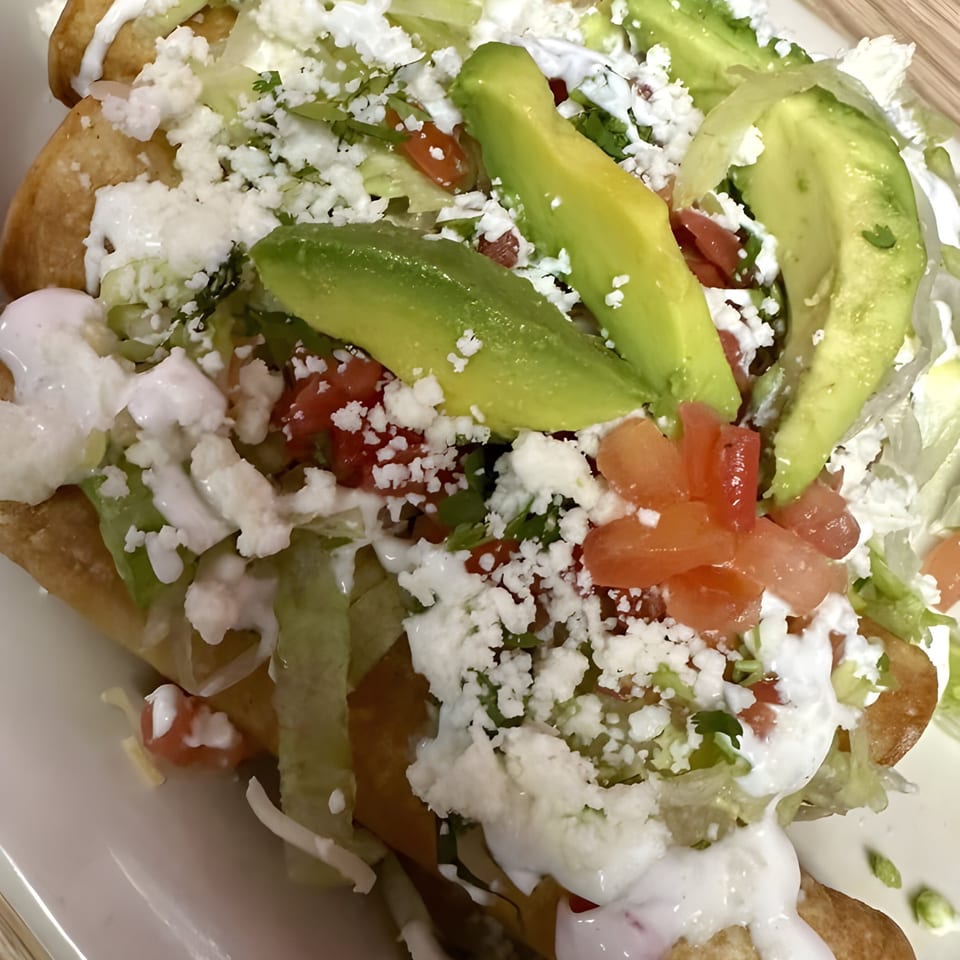 Crispy taquitos topped with shredded lettuce, diced tomatoes, crumbled cheese, avocado slices, and sour cream.